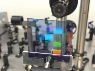 Ein Werkstück des neuen Lasermaterials mit zehn Quadraten, jeweils mit einem anderen Muster von Silberstreifen. Die Farben auf dem Testmuster sind nicht das Laserlicht (der Laser ist auf diesem Foto nicht eingeschaltet), sondern Spiegelungen wie auf einer CD (Foto: Alexei Halpin, TU Eindhoven).