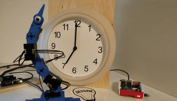 Ein über ein serielles Kabel angeschlossenes Arduino-Board kommuniziert mit Servos.
Als die Uhr nicht mehr funktionierte, beschloss Hendrik, den Roboterarm dazu zu benutzen, die Zeiger zu bewegen, um die Zeit anzuzeigen.
Der Raspberry Pi 3B+ liefert die nötige Rechenleistung, um präzise Positionsanweisungen zu geben, damit die Roboterarme die Zeiger der Uhr imitieren können.
 